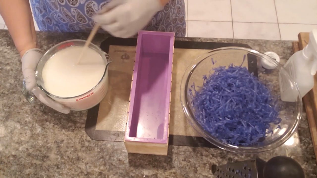 Melted white soap base next to a loaf mold and blue soap shreds