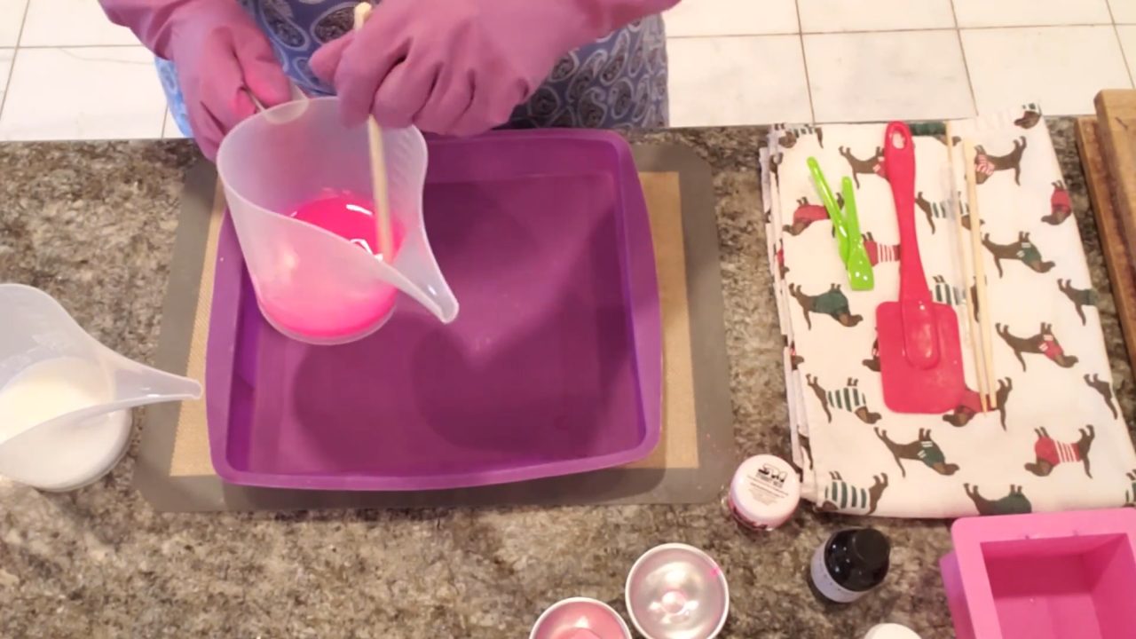 Pouring hot pink clear soap into a purple silicone cake pan