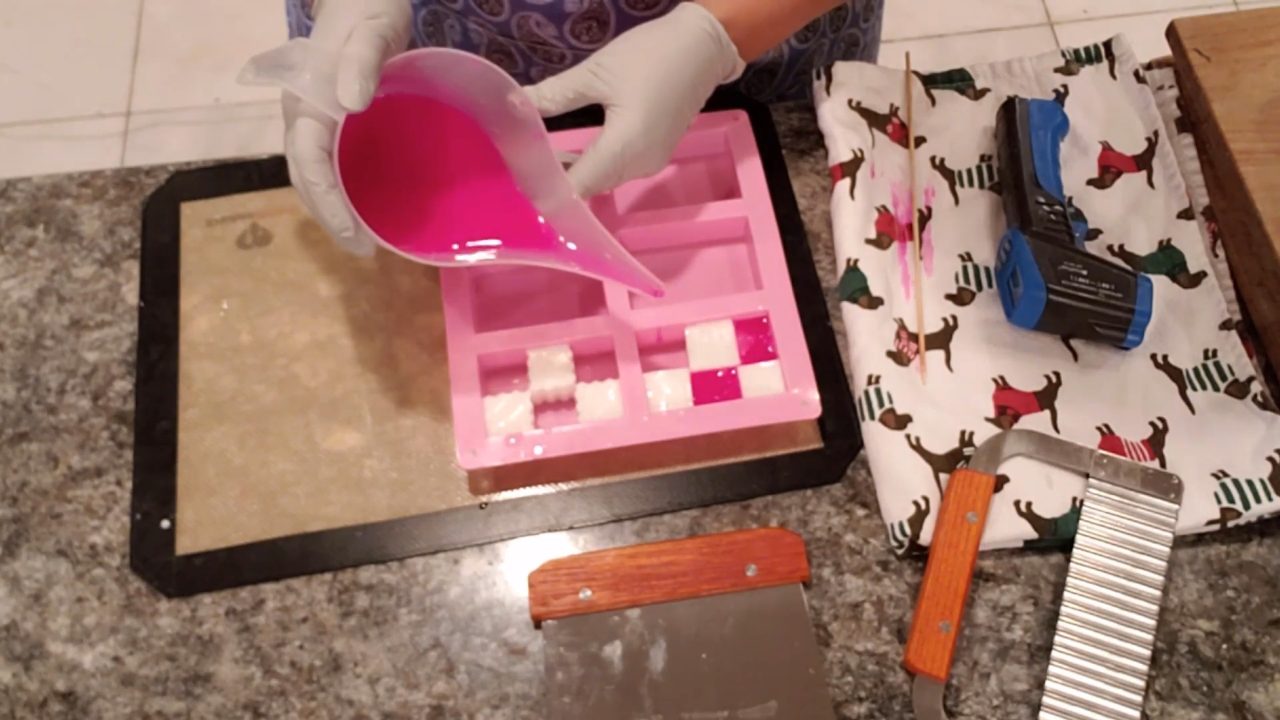 Pouring hot pink melt and pour soap around white soap squares with a funnel cup