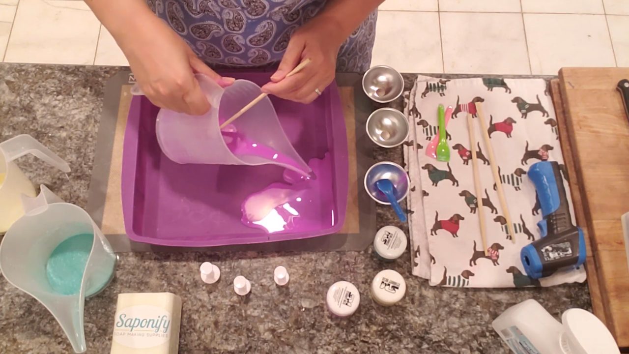 Pouring purple, green and yellow soap into a silicone cake pan