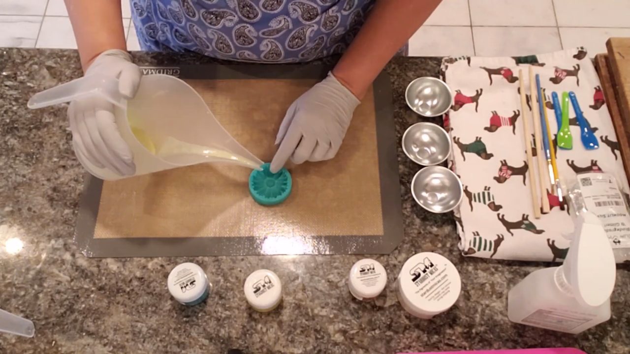 Pouring yellow mica-colored shea butter soap into the center of a daisy mold
