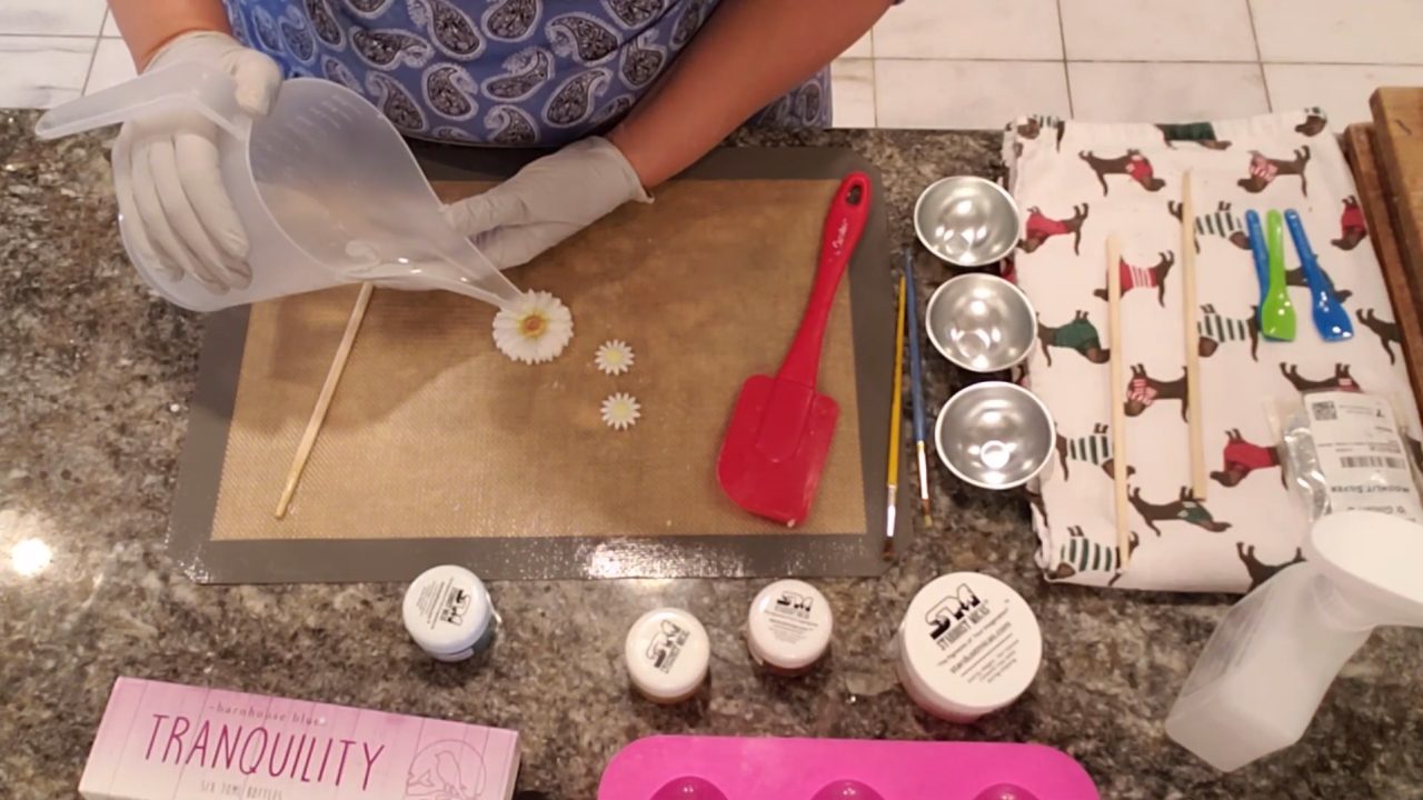 Pouring clear melt and pour soap over the daisy embeds to seal in the mica