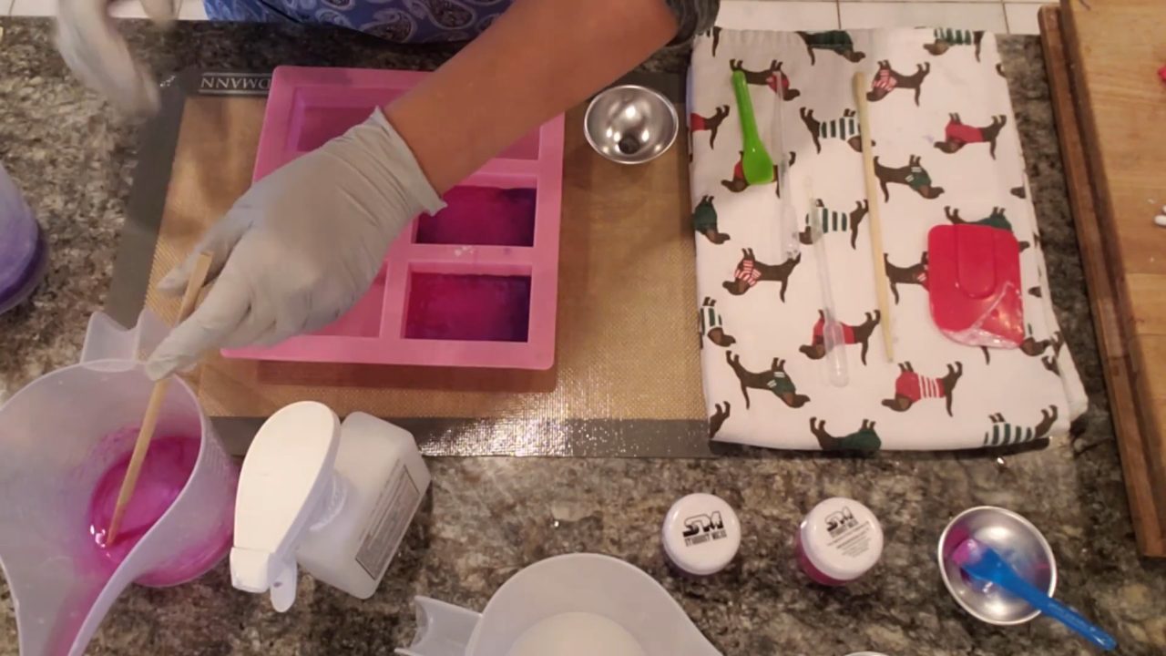 Filling the mold cavities with pink and purple clear soap over the stamped white layer