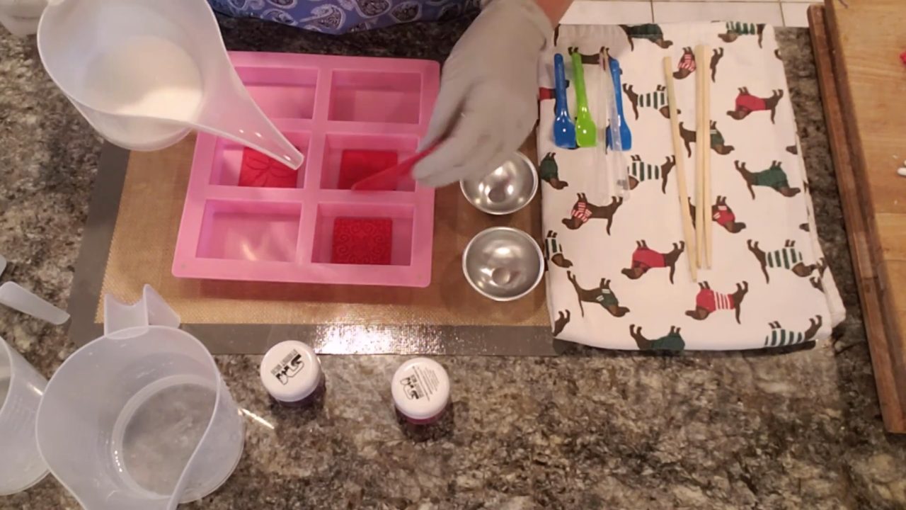 Pouring white shea butter melt and pour soap over a soap embossing stamp