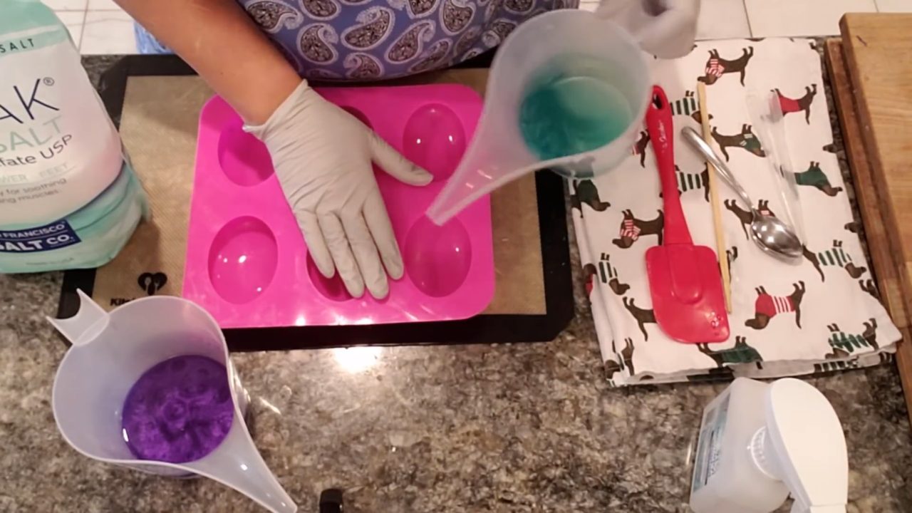 Pouring green soap over Epsom salt in an oval soap mold