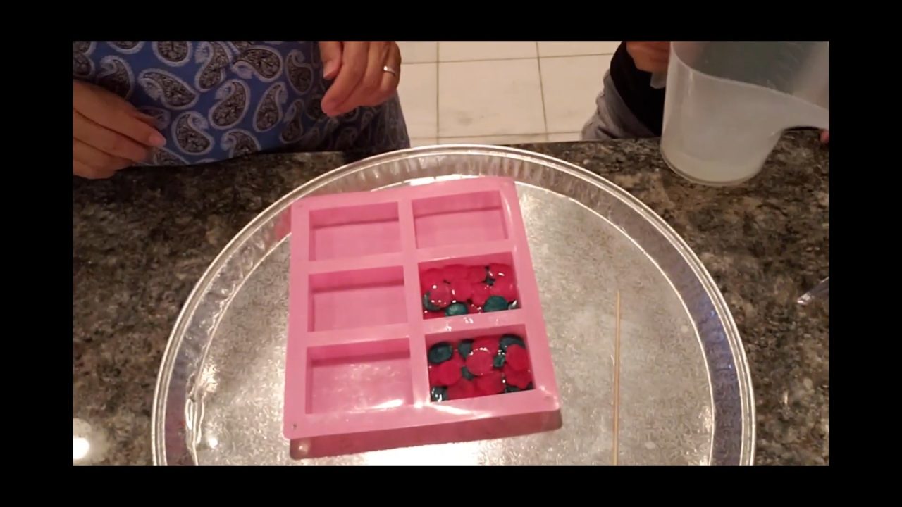Flower embeds arranged in clear soap in a pink silicone bar mold