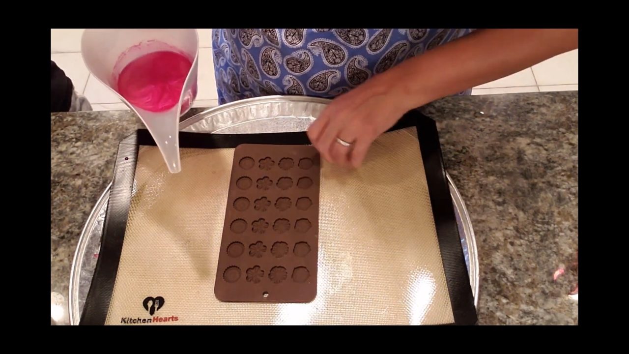 Pouring red mica-colored clear soap over a small flower embed mold on a silicone mat