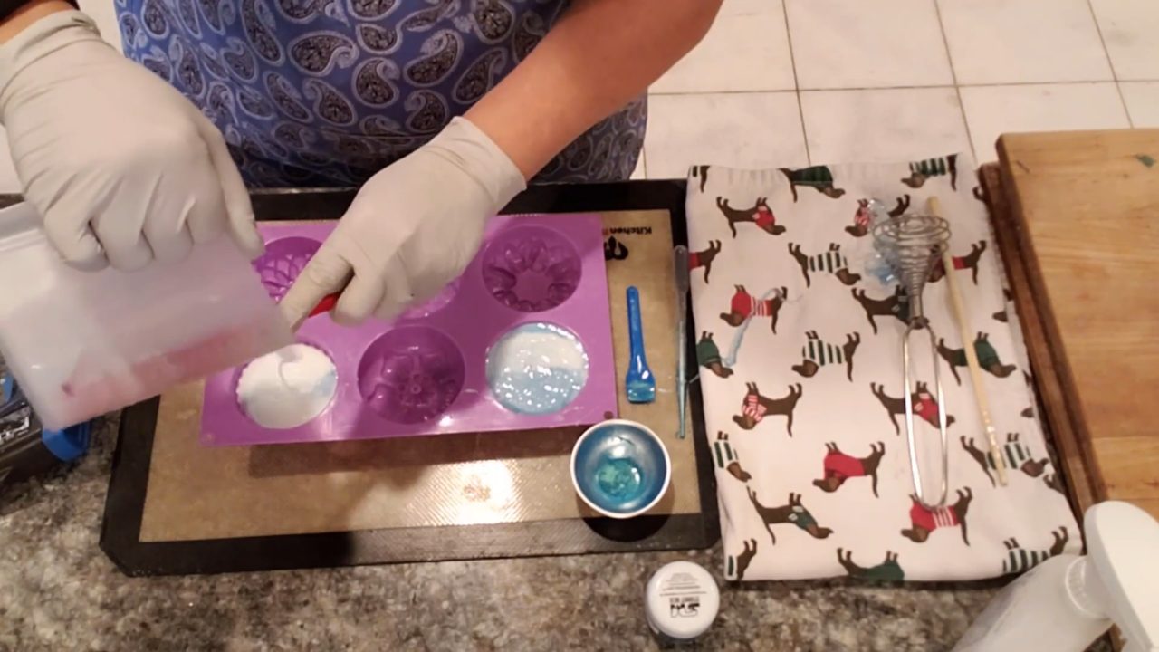Pouring blue swirled shea butter soap into a flower mold