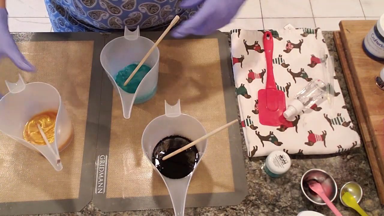Stirring green, gold and black mica-colored clear melt and pour soap in pour cups
