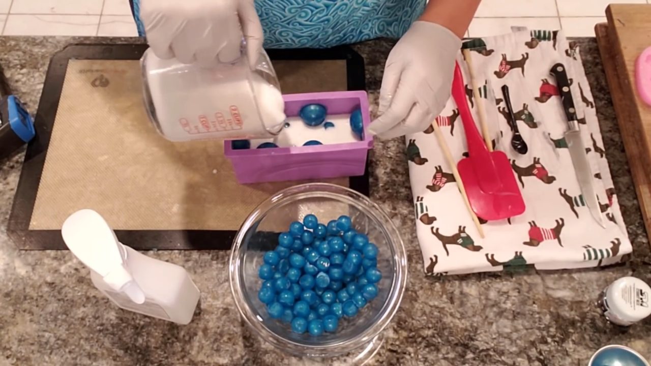 Dropping small blue soap balls into the white shea butter in the loaf mold