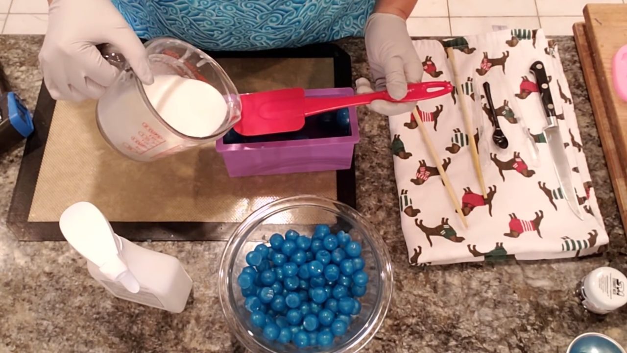 Pouring white shea butter melt and pour soap into the loaf mold with blue dots