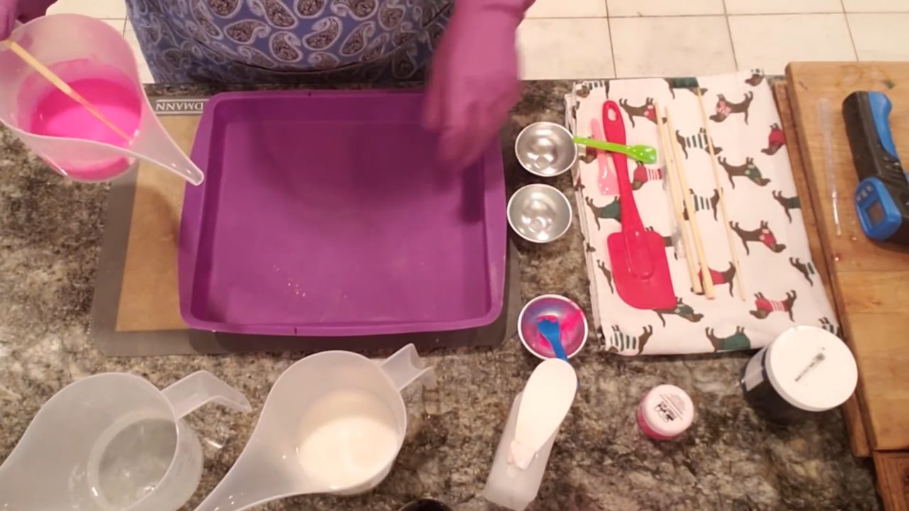 Pouring neon pink shea butter soap into a silicone cake pan