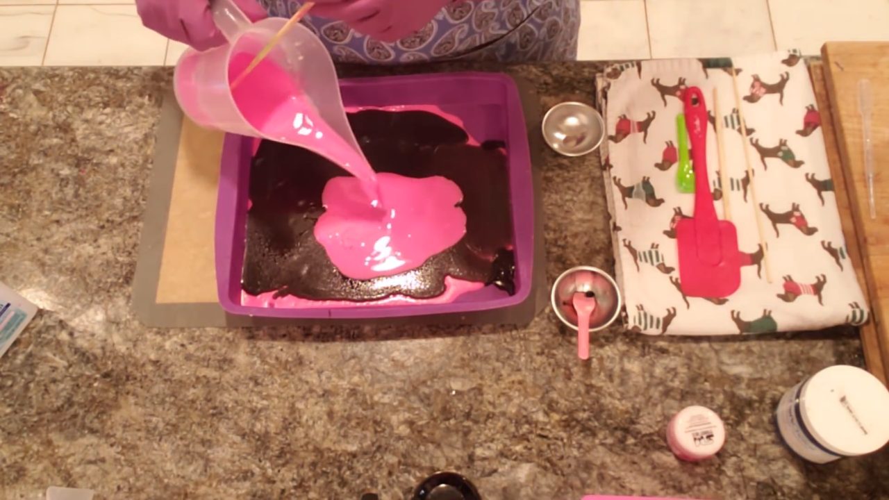 Pouring a second layer of neon pink soap over the charcoal