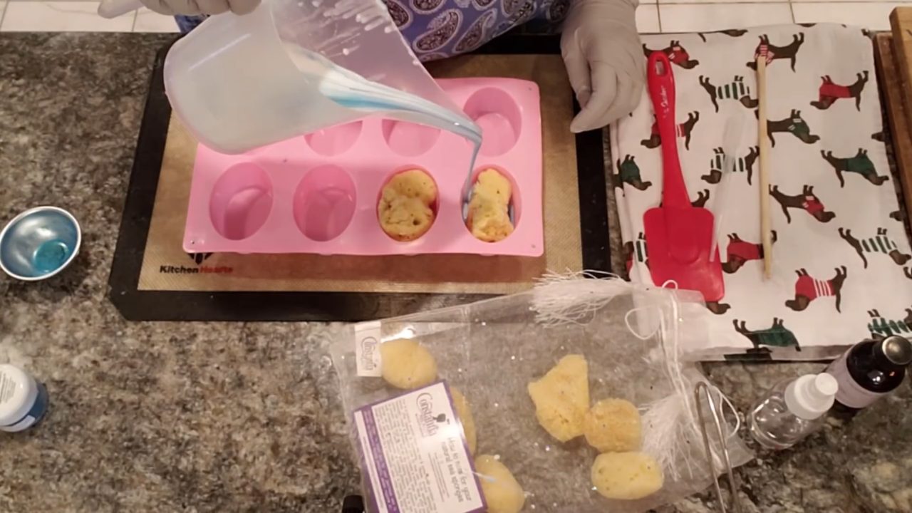 Pouring swirled blue shea butter soap over a sea sponge in the mold