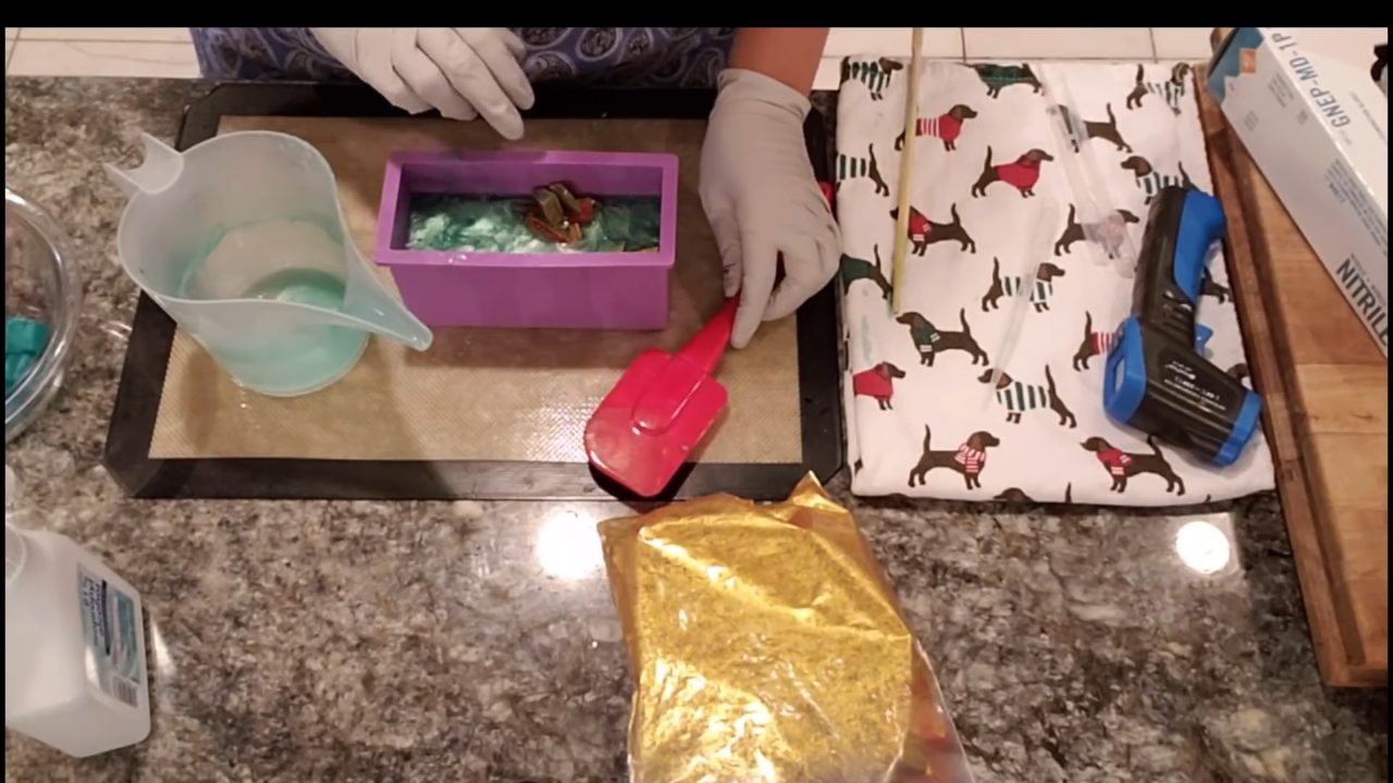 Pouring clear green soap over gold-dusted embeds in a mini loaf mold