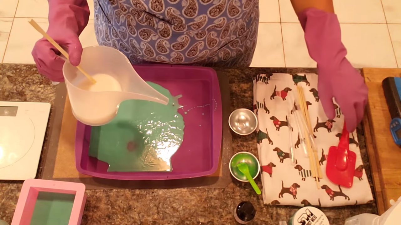 Pouring green shea butter soap into a silicone cake pan to make a slab