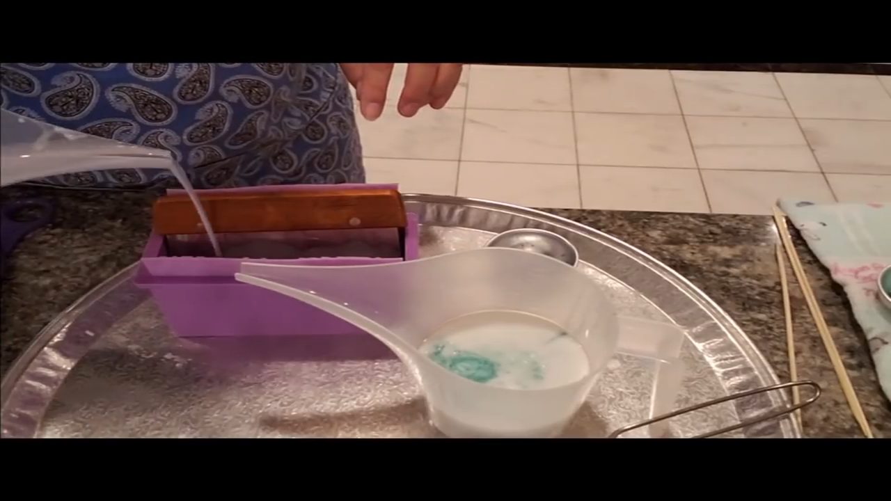 Pouring swirled blue and purple goats milk soap into a mini loaf mold