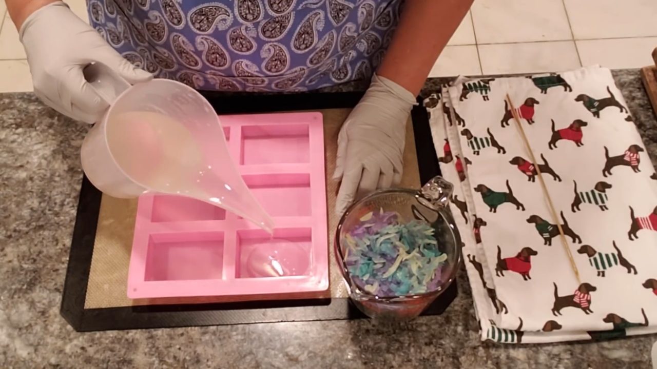 Pouring a thin layer of glittered clear soap into a pink bar mold